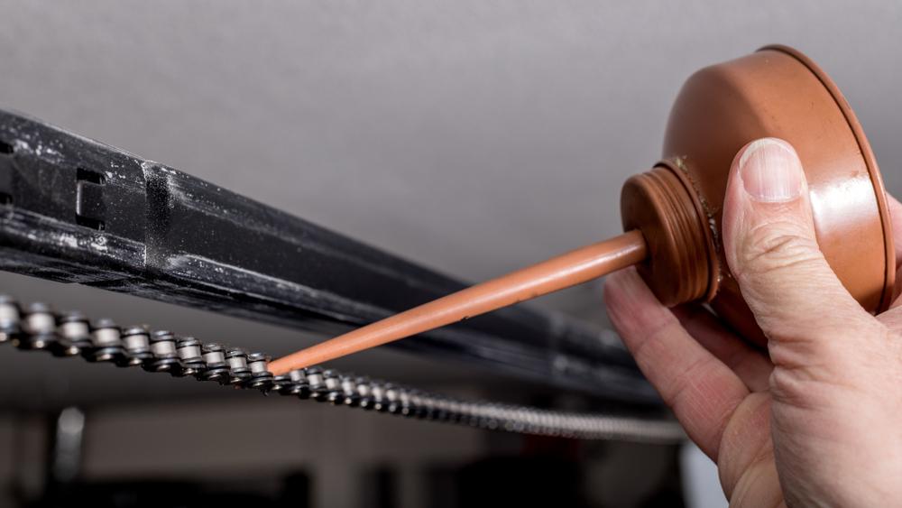A close-up photo of a hand lubricating a garage door with oil.
