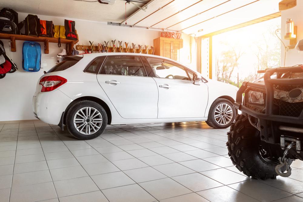 A garage with a white hatchback inside and sun entering the garage door that won’t close.